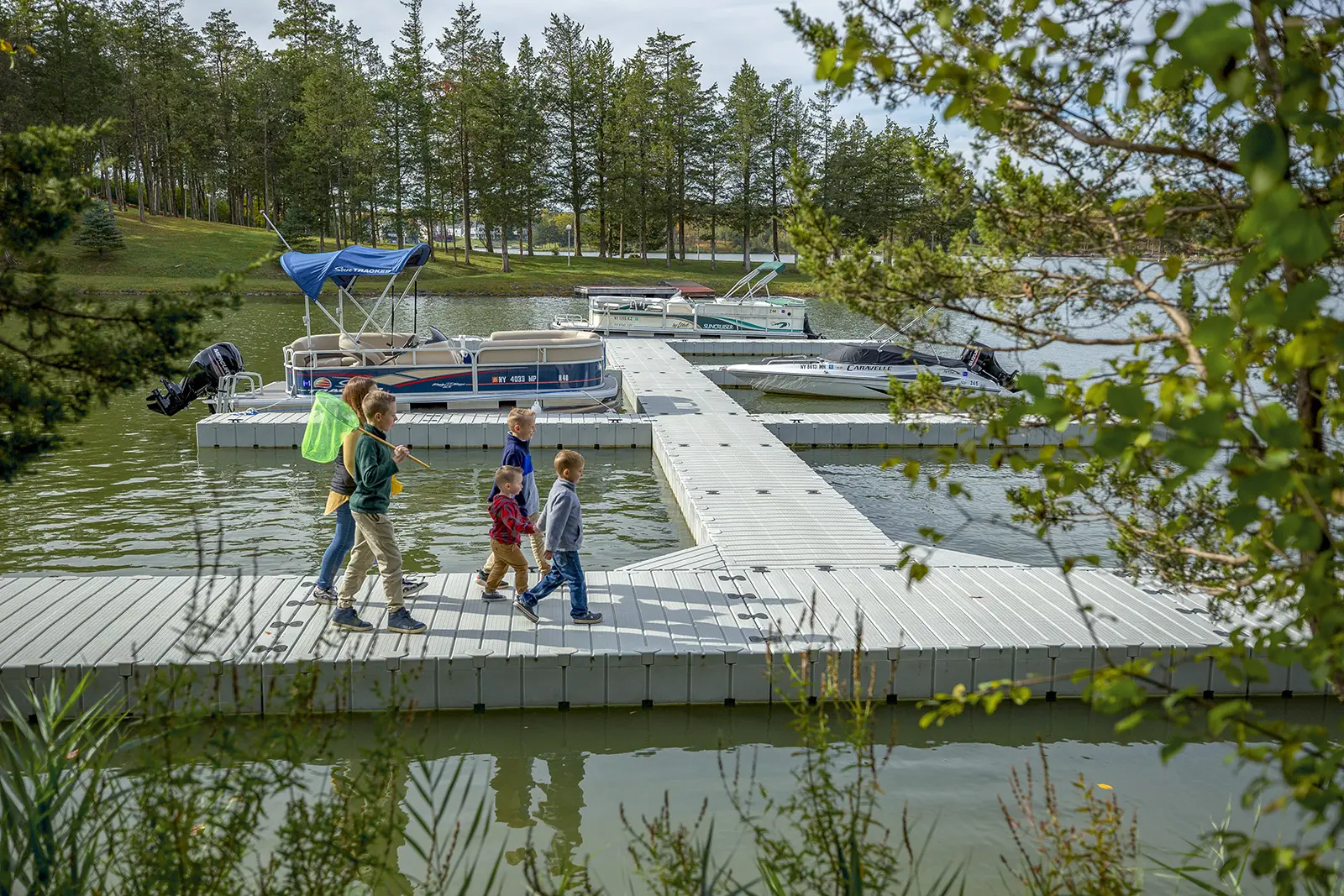 A group of kids walking on the dock with boats parked